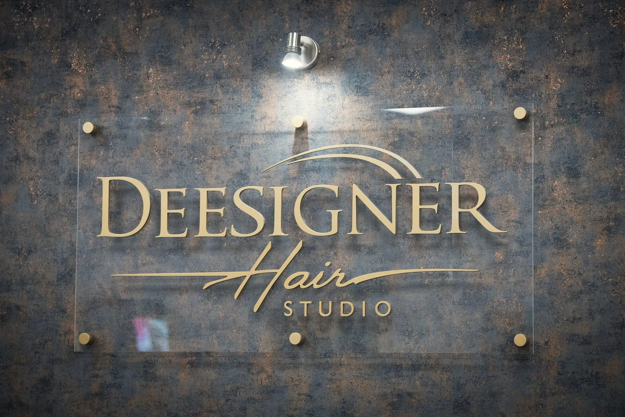 The Deesigner Hair Studio wordmark on the bronze wall inside the salon